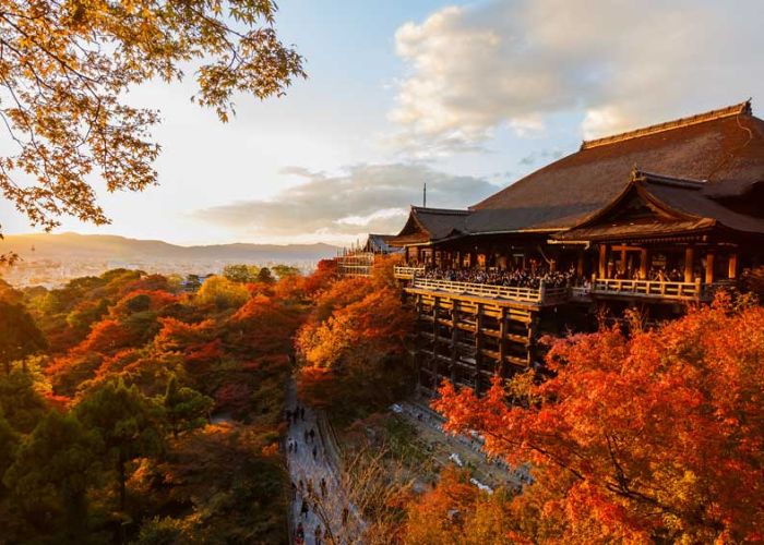 a large tea house on a mountain top in Kyoto, Japan surrounded by trees in brilliant colors of orange, red and yellow with the sun starting to set