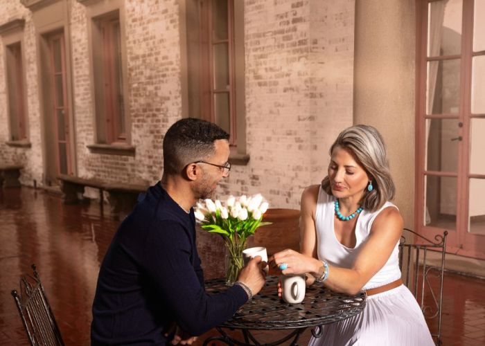 A husband and wife sit together at a bistro table in an old Italian villa on a rainy day